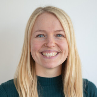 Frau mit blonden langen Haaren und breitem Lächeln.